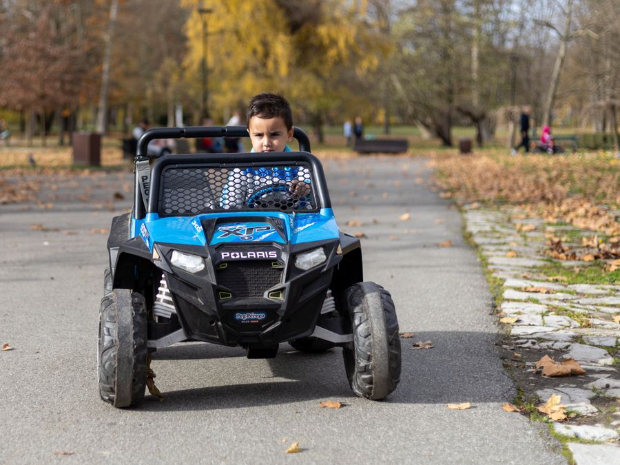 Niño con coche eléctrico en parque otoño